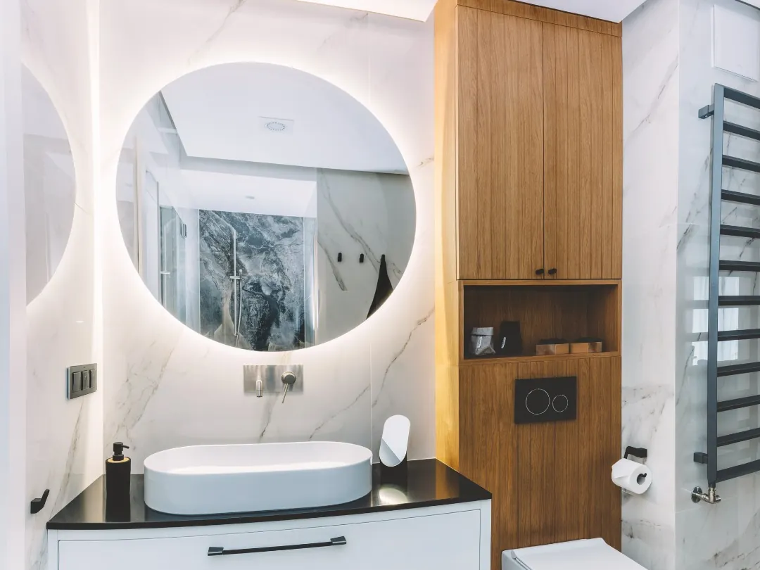 Baño reformado con mueble de madera, espejo redondo y grifería en negro mate